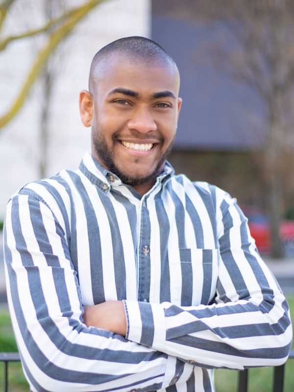 Confident young guy with crossed arms posing on street. Front view of handsome African American man looking at camera. Happiness concept