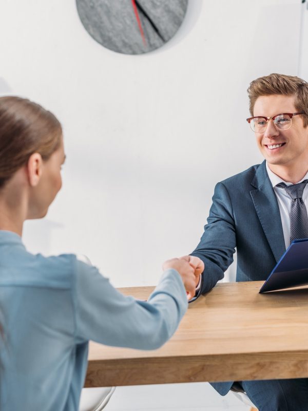 woman-shaking-hands-with-cheerful-recruiter-in-glasses-holding-clipboard