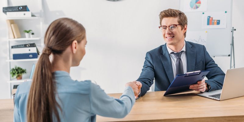 woman-shaking-hands-with-cheerful-recruiter-in-glasses-holding-clipboard